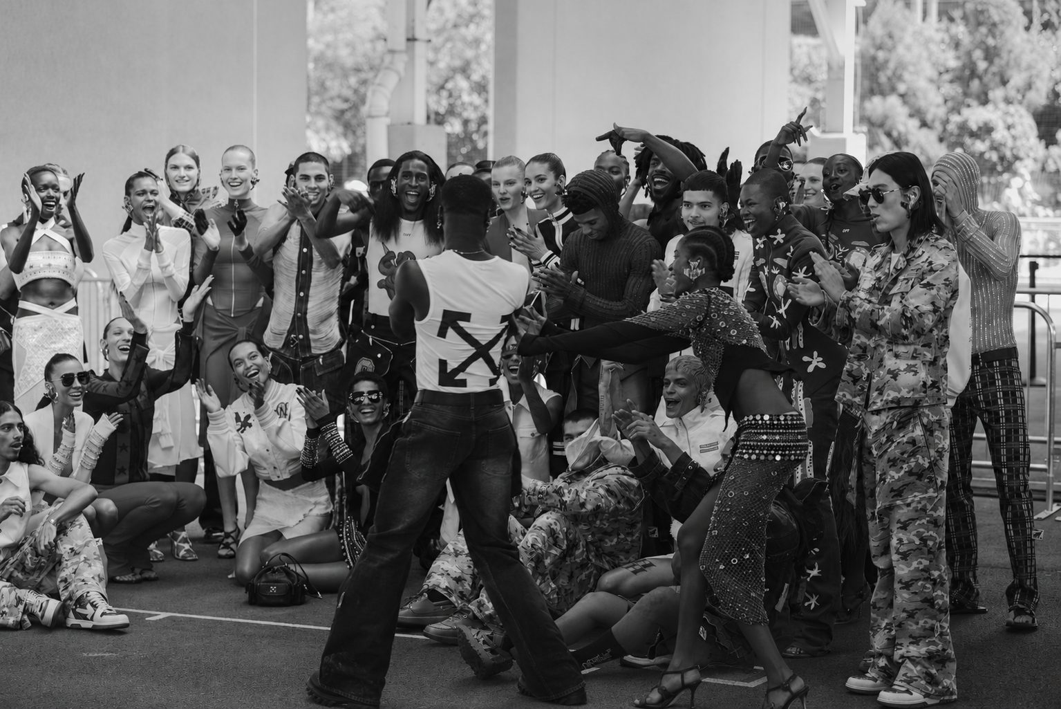 An audience rings a basketball-court runway beneath an Off-White flag, in black and white.