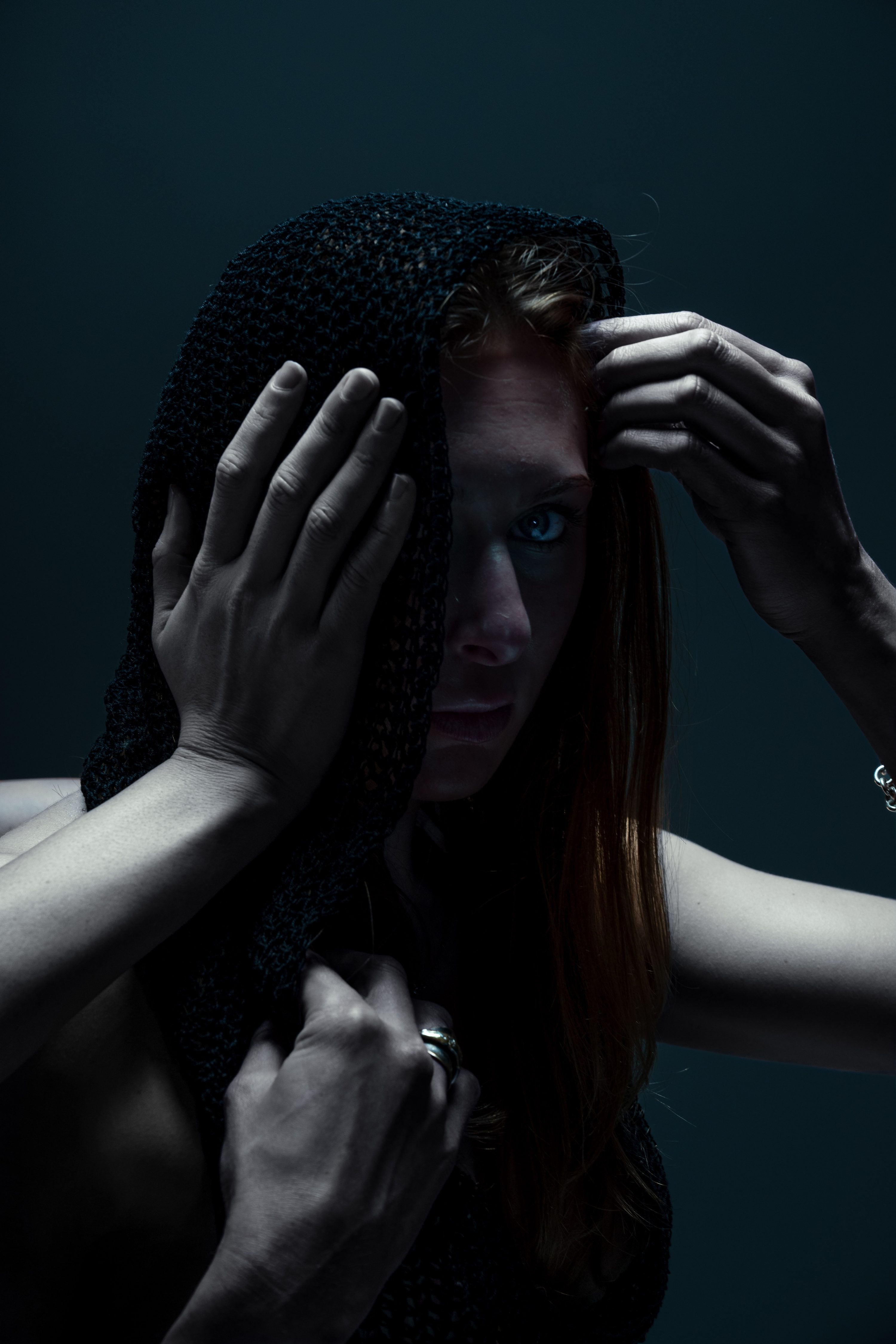 A red-haired woman holds one hand over her eye against a teal backdrop.
